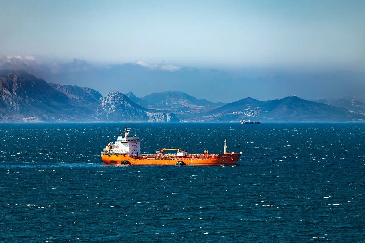 An oil tanker crossing a mountain-flanked shipping strait in daylight