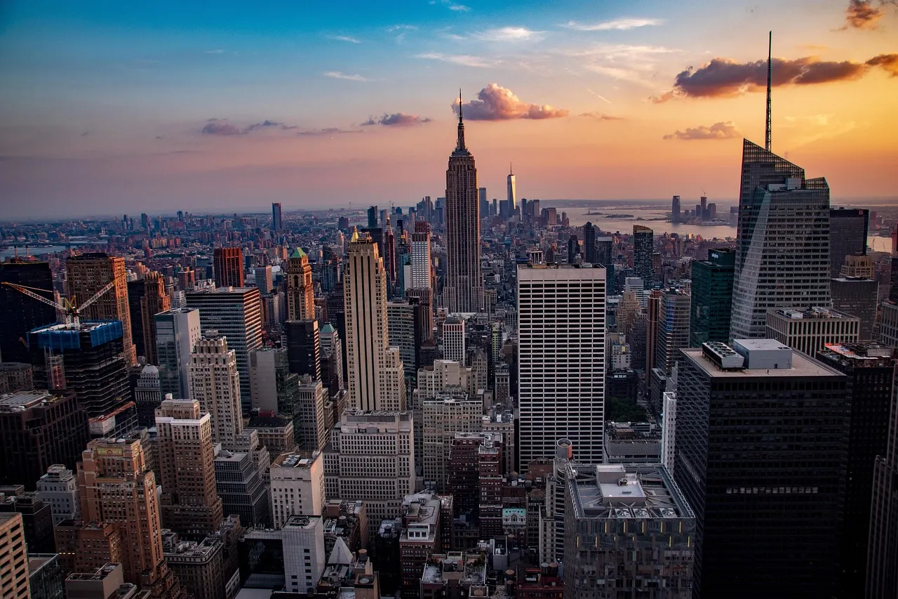 The Manhattan skyline at dusk, the Empire State Building at center and skyscrapers stretching to the horizon under an orange and blue sky.