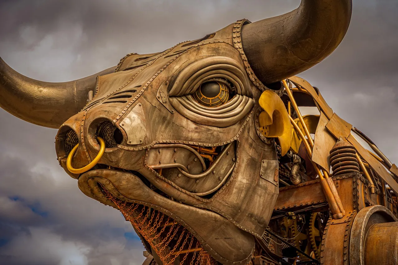 A large mechanical bull sculpture with riveted metal plating and long curved horns, seen from below against a cloudy sky.