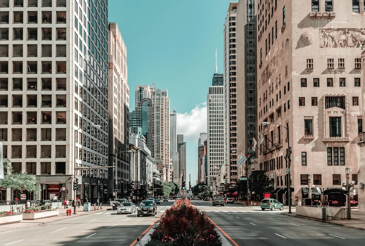 A sunlit downtown avenue framed by tall office towers under a clear sky.