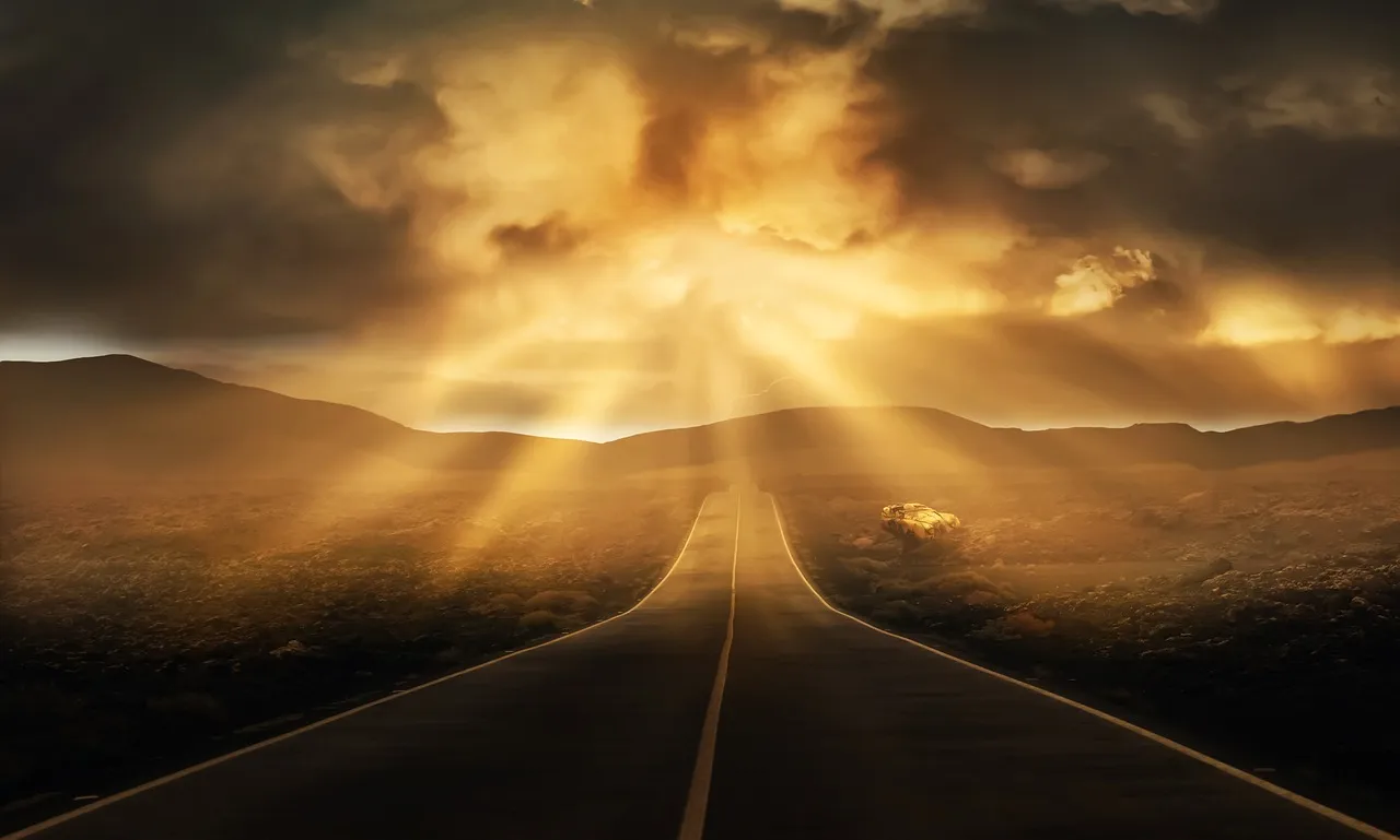 An empty two-lane highway stretching toward distant hills under a dramatic, sunbeam-filled sky at dusk.